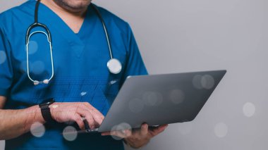 Healthcare professional wearing scrubs and stethoscope uses laptop, symbolizing integration of technology in medical practices and future of patient care clipart