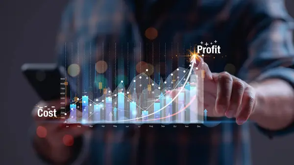 Adamın biri elinde bir cep telefonu tutuyor ve bir işin maliyetini ve kârını gösteren bir grafiğe işaret ediyor.