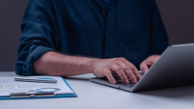 Masasında dizüstü bilgisayarı ve mavi dosyası olan bir adam oturuyor. O elinde bir kalem tutarken dizüstü bilgisayarda yazıyor. Sahne, onun bir proje üzerinde çalıştığını ya da e-posta yazdığını gösteriyor.