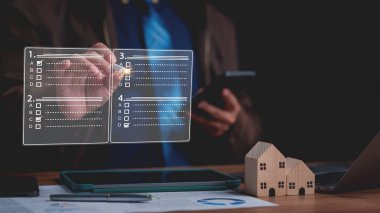 Akıllı telefon tutarken saydam ekranda dijital kontrol listesi kullanan bir birey, ahşap ev modelleriyle birlikte, modern gayrimenkul proje yönetimi ve organizasyonuna örnek olarak