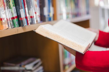 Person is seen exploring pages of book in cozy library, surrounded by shelves filled with various books, inviting sense of curiosity and discovery clipart