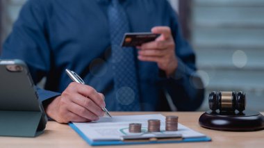 Kredi kartı tutarken profesyonel mali dökümanların incelenmesi, finans ve hukukun kesişmesini sembolize ederken, hukuki otoriteyi temsil eden tokmak