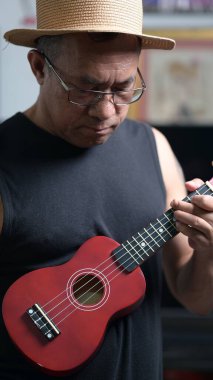 Ukulele çalan Asyalı yaşlı adam.