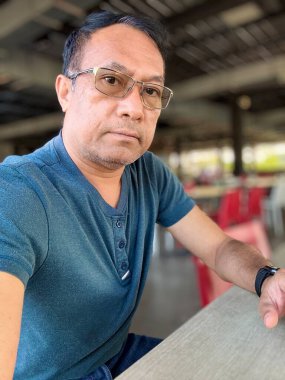 Düşünceli, orta yaşlı bir adam, günlük Teal Shirt 'lü rahat bir selfie çekiyor, doğal ışıklandırma ve şehir ortamında yumuşak odaklı bir özgeçmişi var.