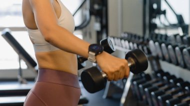 Güçlü Kadın Spor Salonu 'nda Güçlü Vücut Çalışmaları, Spor Sütyeninde Dambıl Eğitimi Ekipmanlarıyla Sağlık Gücü Gösteriyor.