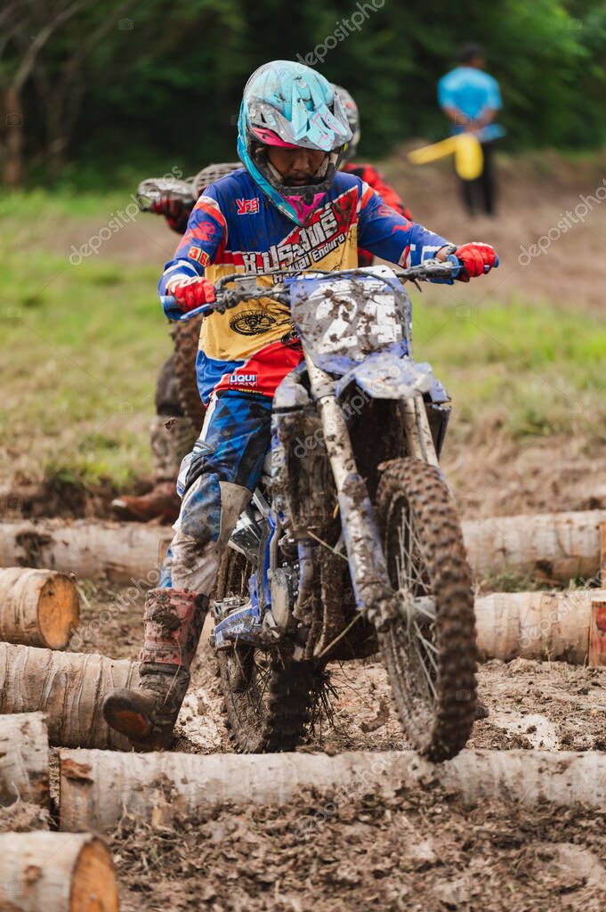 Songkhla, Hatyai, Thailand May 25, 2025: Mastering the Mud, Muddy Motocross Race Rider Conquers Terrain, Wheel Over Logs