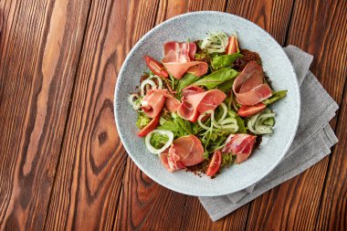 Prosciutto ile lezzetli salata, taze kiraz domatesleri, salata karışımı, marine edilmiş soğan halkaları ve gri kasede servis edilen chia tohumları..