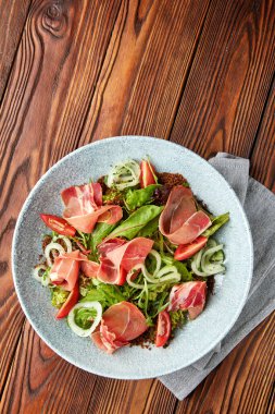 Prosciutto ile lezzetli salata, taze kiraz domatesleri, salata karışımı, marine edilmiş soğan halkaları ve gri kasede servis edilen chia tohumları..