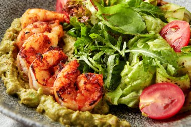 Soslu ızgara karides, salata, ızgara kabak ve gri kasede taze vişneli domates..