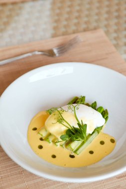 Sağlıklı kahvaltı, holandez soslu haşlanmış yumurta kuşkonmazla servis edilir ve bitkisel yağla süslenir.