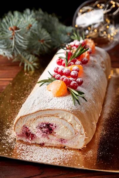 Festive Christmas meringue roll with cherries decorated with cranberries, citrus and rosemary on wooden table.