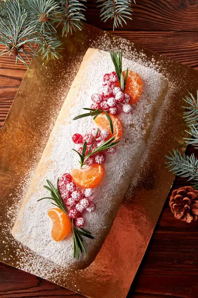 Festive Christmas meringue roll with cherries decorated with cranberries, citrus and rosemary on wooden table.