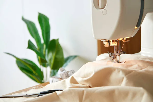 Close up view of sewing machine with piece of natural beige cotton fabric, seamstress workplace.