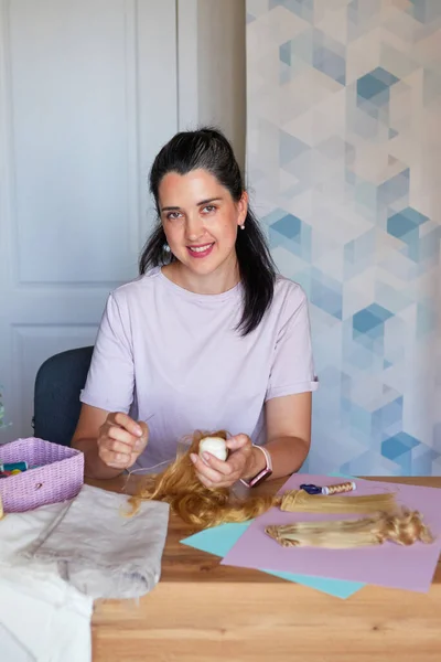 stock image Portrait of creative young adult woman making handmade doll, sewing hair to doll.