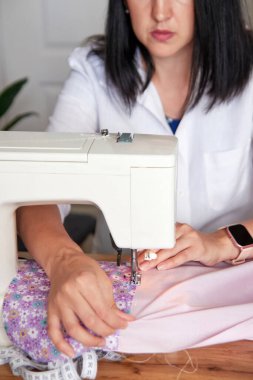 Genç yetişkin terzi dikiş makinesinde çalışıyor, renkli kumaşlar dikiyor..