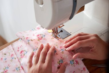 Dikiş makinesinde çalışan kadın elleri, renkli kumaşlar dikiyorlar..