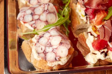 Rihotta, prosciutto, ançüez, domates, roka ve ahtapot dilimli çeşitli bruschetta manzarası..