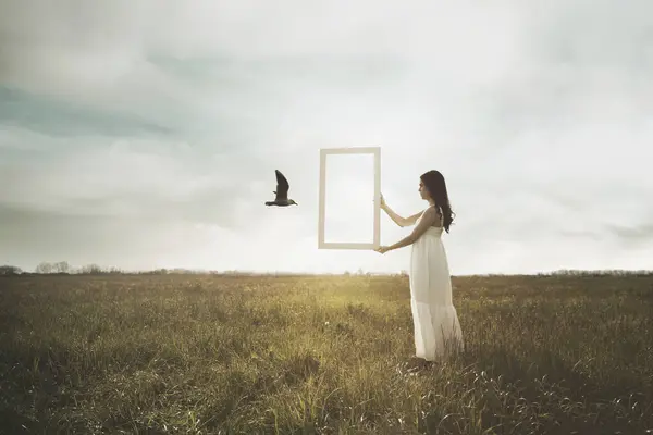 stock image bird escaping through a surreal window held by a woman, concept of freedom