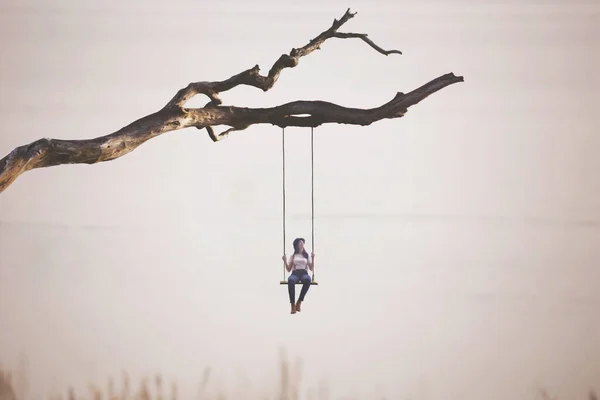 stock image surreal woman swings on a swing hanging from a branch, concept of freedom and precariousness