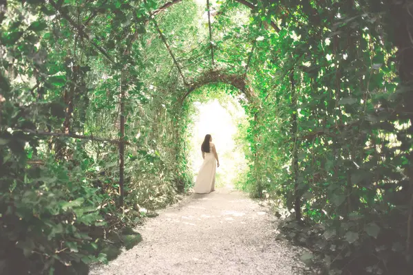 优雅的年轻女子兴高采烈地走向由茂密的植物构成的隧道出口 图库图片