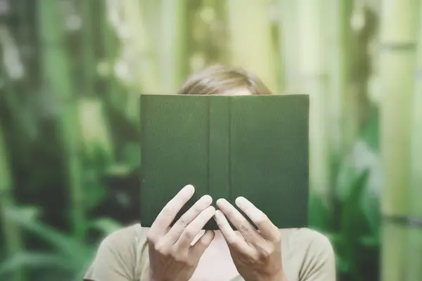 一个人的超现实时刻 在他的面前放着一本绿皮书 与周围的自然融合在一起 然后消失了 免版税图库图片