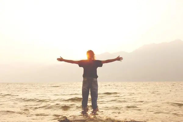 Stock image woman with open arms welcomes the warmth of the light of the setting sun on the banks of a lake