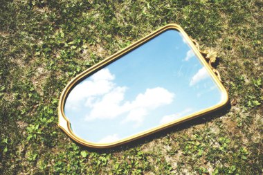 mirror in a meadow reflects a surreal sky with clouds, abstract concept clipart