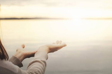 Kişi açık ellerle güneşin sıcaklığını ve enerjisini hoş karşılar.