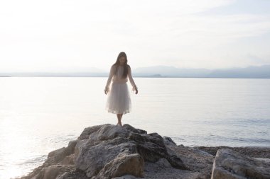 Kadın, arkası muhteşem deniz manzarasına dönük olarak kayanın üzerinde yürüyor.