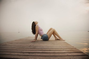 Young girl lying and relaxed takes a breath on a pier facing the sea