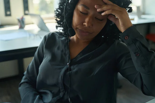 疲れた多人種女性コールセンターのオペレーターテーブルに座って頭痛の種に苦しんで — ストック写真