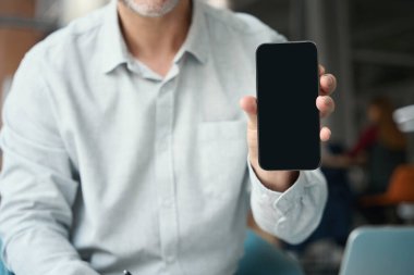 Günlük kıyafetli bir adam elinde bir telefon tutuyor ve bir aletin ekranını gösteriyor.