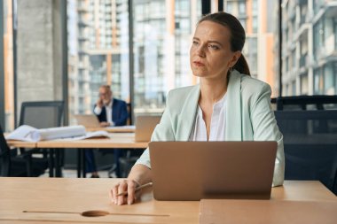 Ciddi bir kadın iş yerinde akıllı telefondan iletişim kurarken elinde defterle masada oturuyor.