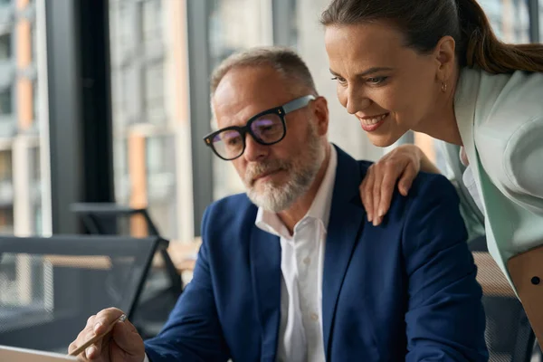 戴眼镜的生意人正在向一个微笑的女同事展示笔记本电脑屏幕 这个女同事正挽着他的肩膀 — 图库照片