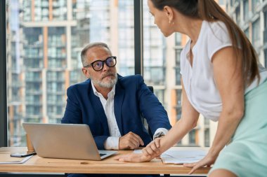 Olgun adam dizüstü bilgisayarda otururken kadın masanın üzerinde oturuyor ve o da onun elini tutuyor.