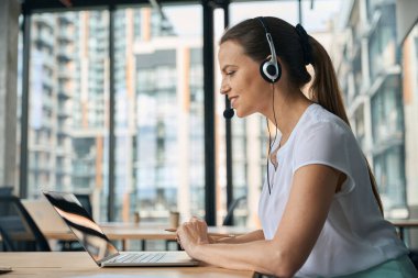 Neşeli kadın masada otururken defter ve kulaklıkla iletişim kuruyor.