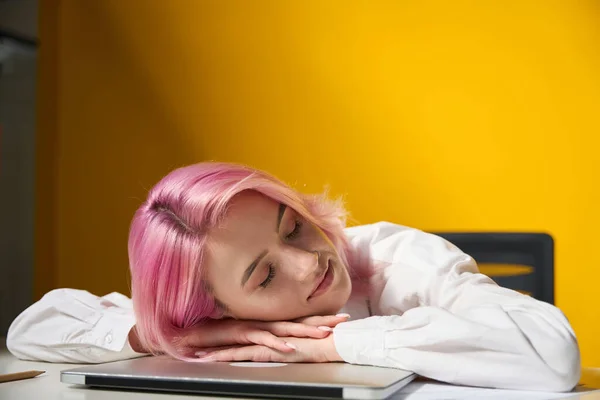 有一头粉色头发的女人坐在办公室的桌子旁边 躺在笔记本电脑上 黄色明亮的背景 — 图库照片