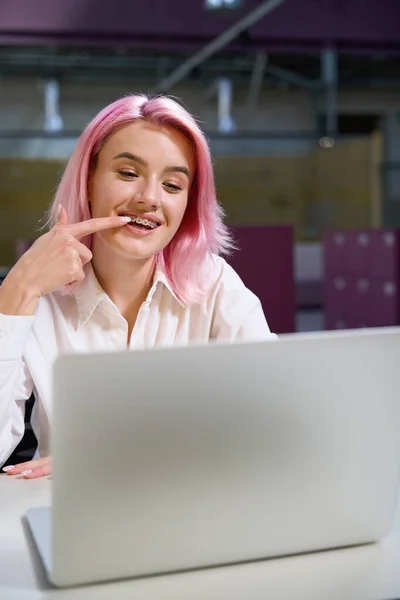 美しいです女性とともにピンクの髪座っていますテーブルの上にノートパソコンとビデオ通話を持っています歯医者 — ストック写真