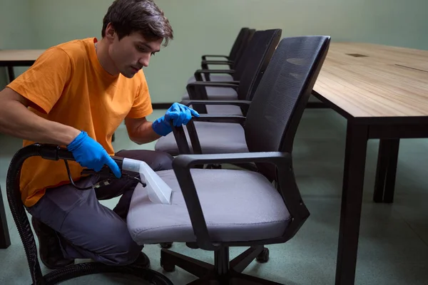 オフィス家具に布張りの掃除機を使用したゴム手袋の注目すべき若い男 — ストック写真