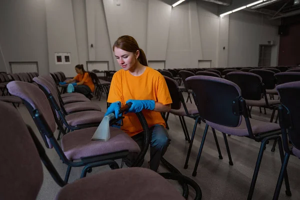 在同事们的帮助下 细心的年轻女人在椅子上用吸尘器清洁室内装潢 — 图库照片