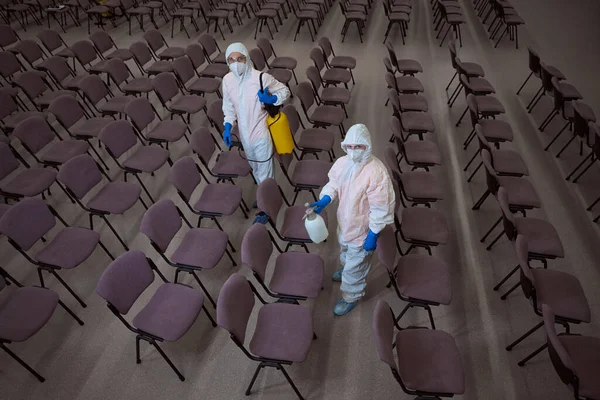 Two professional cleaners in overall protective gear and with chemical supplies in hands looking at the camera