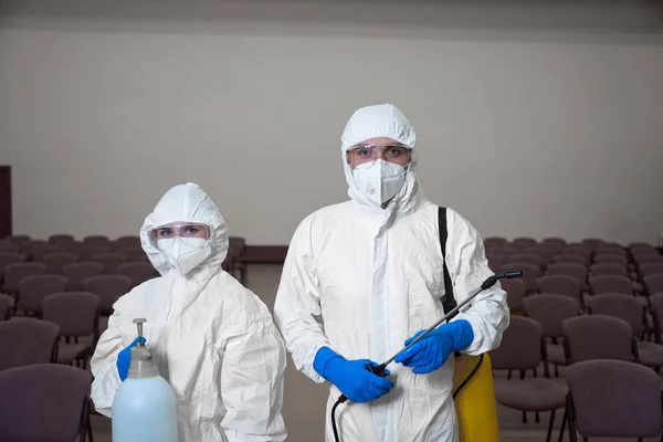 Waist-up photo of two cleaners in overall protection suits and goggles posing with cleaning equipment
