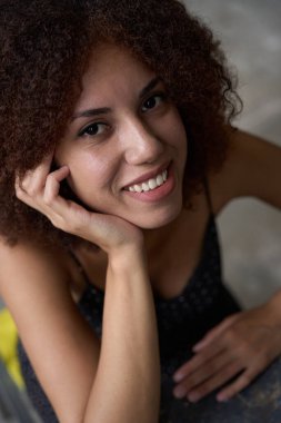 Çekici esmer kadının yakın plan fotoğrafı başını eline dayayıp gülümseyerek kameraya bakıyor.