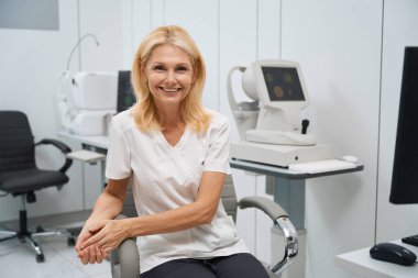 Tıbbi giysiler içindeki mutlu doktor hastanede tıbbi malzemelerle birlikte dolapta oturuyor.