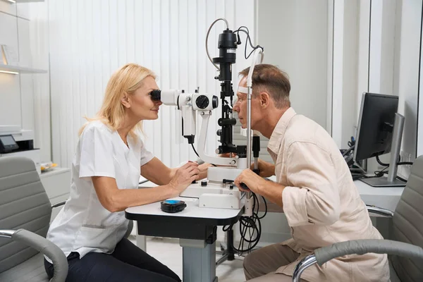 stock image Doctor in white coat sitting at the table opposite the patient and using slit lamp to perform cycloscopy