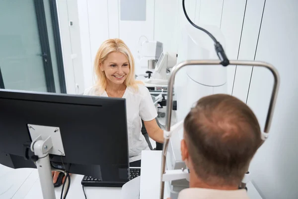 Beyaz Önlüklü Gülümseyen Doktor Bilgisayarın Başında Oturuyor Göz Muayenesi Yapıyor — Stok fotoğraf