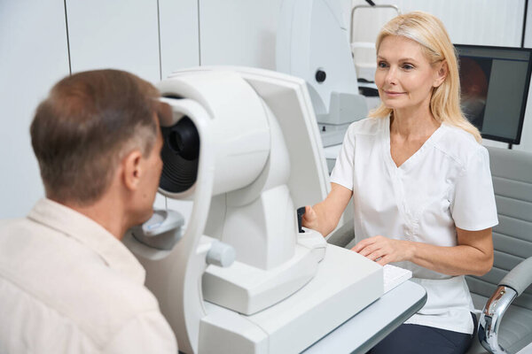 Oculist in white coat sitting at the computer and performing eye examination with optical biometer