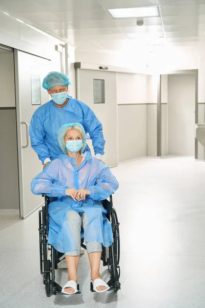 파란색 보호용 양복을 남자는 휠체어에 수술을 여자를 태운다 — 스톡 사진