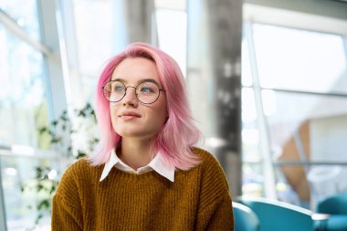 Ofisteki kanepede oturmuş pencereye bakan pembe saçlı güzel bir kadın.