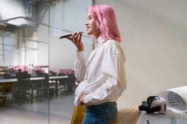 Pembe saçlı bir kadın telefonu tutuyor. Müşteri ile birlikte çalışıyor, ileriye bakıyor ve gülümsüyor.